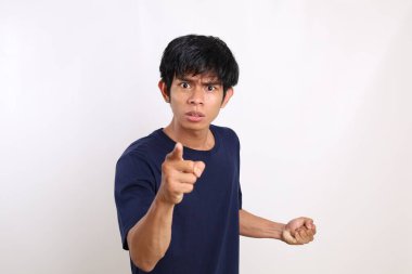 Kamerayı işaret edip bakarken ayakta duran Asyalı öfkeli genç adamın portresi. Beyazda izole edilmiş