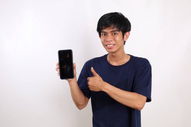 Asyalı genç adam boş bir cep telefonu ekranı sunarken ve başparmağını kaldırırken...