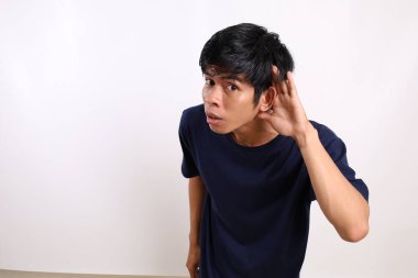 Genç Asyalı adam elini kulağının yakınına koydu. Dedikodu konsepti. Kopyalama alanı ile beyaz arkaplanda izole