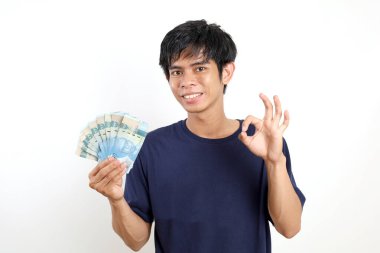 Genç Asyalı adam elinde Endonezya banknotlarıyla el hareketleriyle ayakta duruyor. Beyazda izole edilmiş
