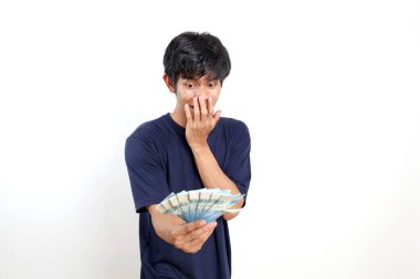 Endonezya banknotları elinde tutarken şaşırmış ve şaşırmış Asyalı genç bir adam. Beyazda izole edilmiş