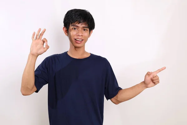 Happy Asian Young Man Standing While Pointing Sideways Showing Okay — Stock Photo, Image