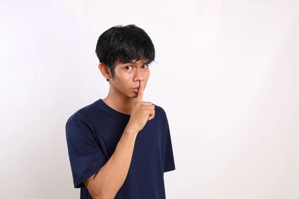 年轻的亚洲男子站在那里 用手指捂住嘴唇 站在白色的背景下 — 图库照片