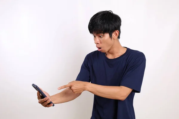 携帯電話を持ちながら立っている若いアジア系の男に驚いた 白に隔離された — ストック写真