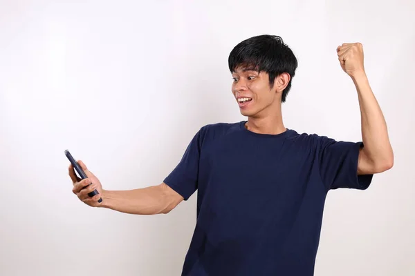 快乐的亚洲年轻人一边站着 一边用拳头从他的手机里得到好消息 与白种人隔离 — 图库照片