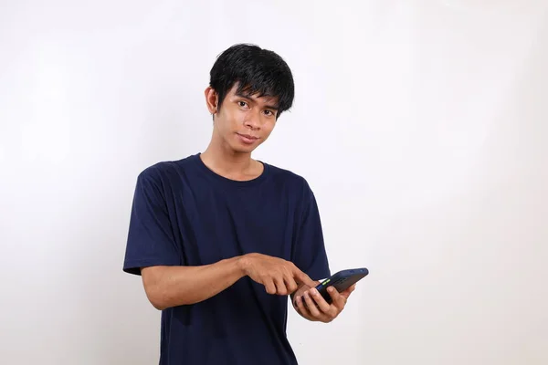 一个年轻的亚裔男子拿着手机站在那里 用手指着手机的画像 与白种人隔离 — 图库照片