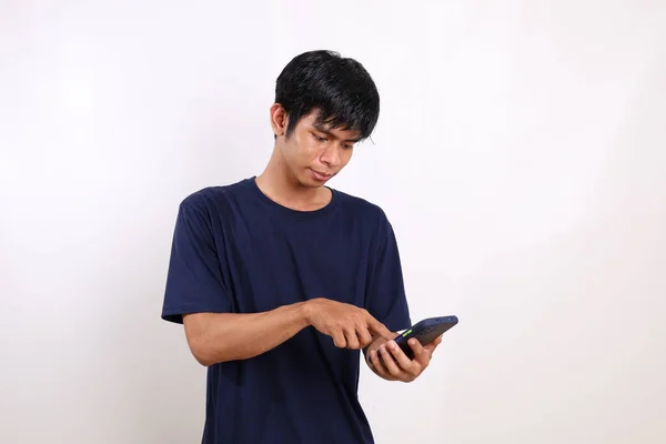 携帯電話を持っている間に立っている若いアジアの男の肖像画とそれに彼の指を指す 白に隔離された — ストック写真