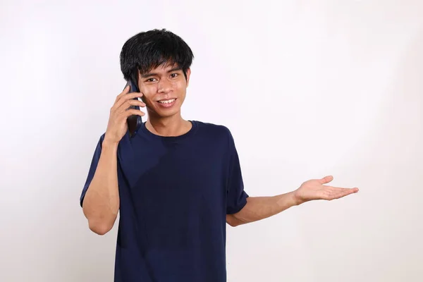 電話で話していると 彼の横に何かを提示しながら 幸せな若いアジアの男 コピースペースと白い背景に隔離されています — ストック写真