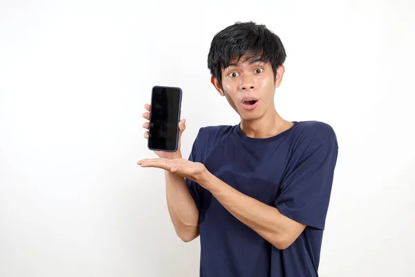 空白の携帯電話の画面を提示しながら立っているアジアの若い男の幸せな驚きの表現 白に隔離された — ストック写真