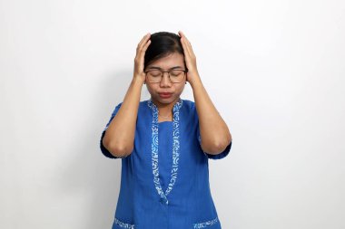 Stresli genç Asyalı kadın başını tutarken ayakta duruyor. Beyaz arkaplanda izole