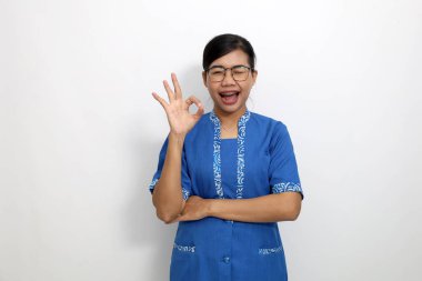 Tamam el hareketi yaparken ayakta duran etkileyici genç Asyalı kadın. Beyaz arkaplanda izole