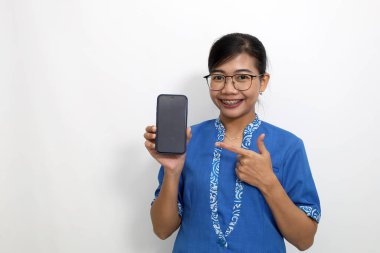 Genç Asyalı öğretmen boş bir cep telefonu ekranını gösterirken ya da sunarken ayakta duruyor. Kopyalama alanı ile beyaza izole edilmiş