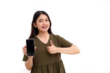 Asyalı mutlu bir kadın boş bir cep telefonu ekranı ve baş parmağını kaldırarak ayakta duruyor. Beyazda izole edilmiş