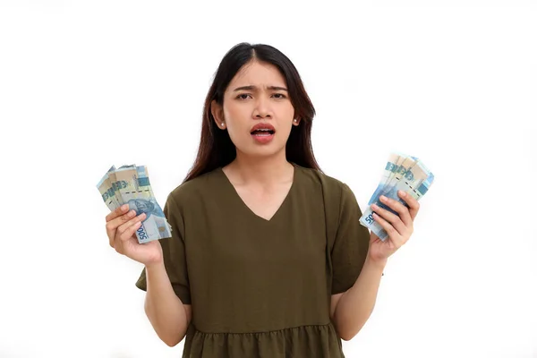 stock image Confused young asian woman standing while holding Indonesian banknotes, Isolated on white background