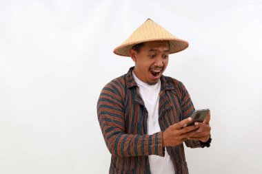 Mutlu Asyalı çiftçi cep telefonundan iyi haberler alırken ayakta duruyor. Beyazda izole edilmiş