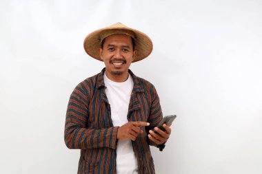 Happy asian farmer standing while pointing his cell phone. Isolated on white background with copyspace clipart