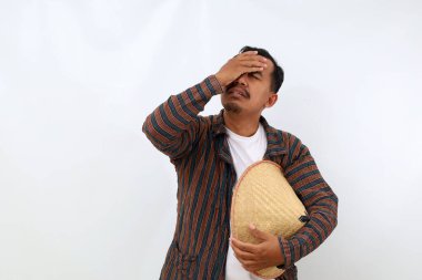 Yorgun ve stresli Asyalı çiftçi başını tutarken ayakta duruyor. Beyaz arkaplanda izole