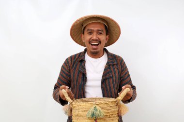 Boş bir sepeti tutarken mutlu Asyalı çiftçi ayakta duruyor. Beyaz arkaplanda izole
