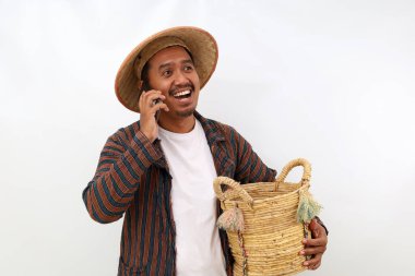 Happy asian farmer standing while talking on the phone and holding a basket. Isolated on white background clipart