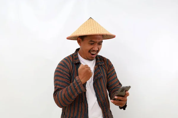 stock image Happy Asian farmer standing while holding a cell phone and clenching his hand. Isolated on white