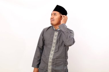 Düşünceli Asyalı Müslüman adam başını kaldırıp yukarı bakarken ayakta duruyor. Beyaz arkaplanda izole