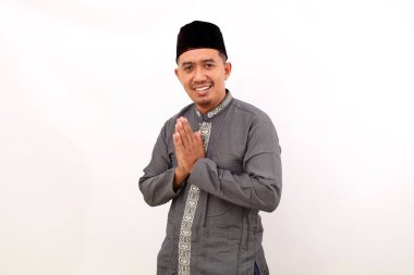 Mutlu Asyalı Müslüman adam el hareketleriyle ayakta duruyor. Beyaz arkaplanda izole