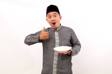 Heyecanlı Asyalı Müslüman adam parmaklarını gösterirken boş bir tabak tutuyor. Beyaz arkaplanda izole
