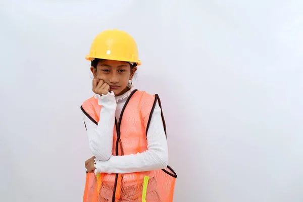 Sad and sluggish Asian little girl in the construction helmet as an engineer feeling tired. Isolated on white