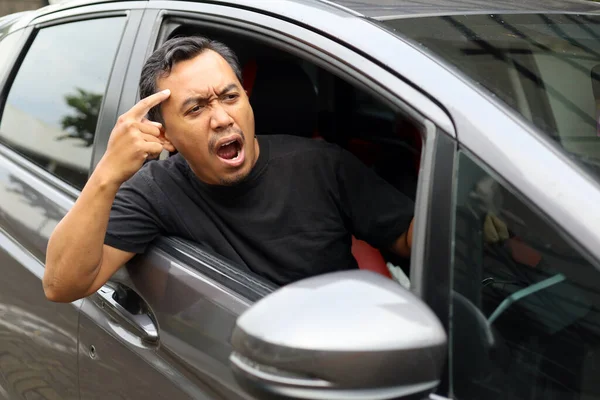 Angry asian man driving car. Arguing and gesturing with something in front his car