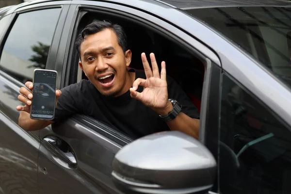 Happy asian driver showing his cell phone screen and showing okay hand gesture in his car
