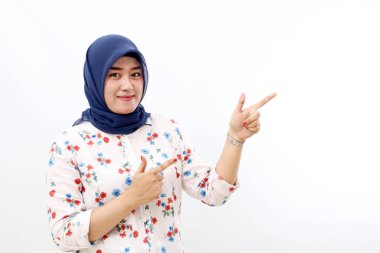 Happy asian veiled woman standing while pointing sideways. Isolated on white background with copyspace