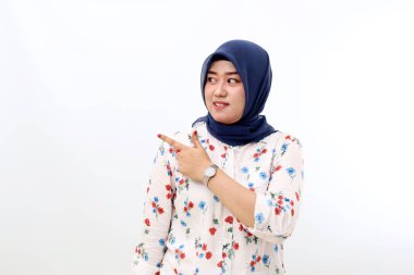 Happy asian veiled woman standing while pointing sideways. Isolated on white background with copyspace