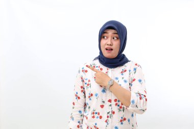Surprised asian veiled woman standing while pointing sideways. Isolated on white background with copyspace