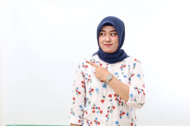 Happy asian veiled woman standing while pointing sideways. Isolated on white background with copyspace