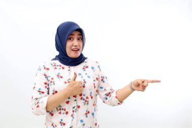 Asian veiled woman standing while pointing sideways and showing thumbs up. Isolated on white