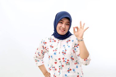 Cheerful asian muslim woman standing while showing okay hand gesture. Isolated on white background