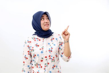 Happy asian muslim woman standing while pointing something above. Isolated on white background