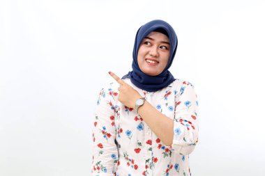 Happy asian muslim woman standing while pointing and glancing sideways. Isolated on white background