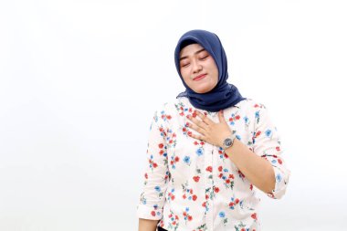 Relieved asian muslim woman standing while holding her chest. Relaxed, calm, peaceful concept