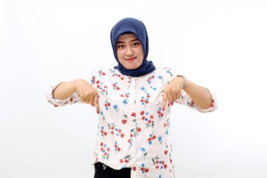 Happy asian muslim woman standing while presenting something in front her. She is pointing down.