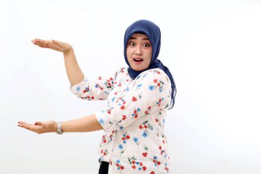 Surprised asian muslim woman standing while presenting something on her hands. Isolated on white