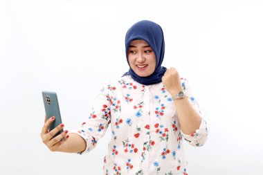 Joyful asian muslim woman standing while holding a cell phone. Isolated on white background