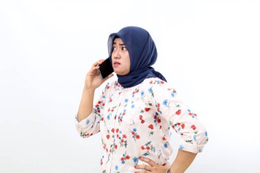 Serious asian muslim woman standing while talking on the phone. Isolated on white background