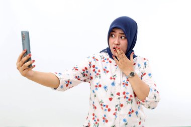 Shocked asian muslim woman standing while getting a news from her phone. Isolated on white