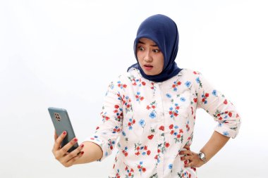 Shocked asian muslim woman standing while reading news from her phone. Isolated on white background