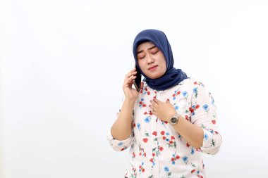 Relieved asian muslim woman talking on the phone while holding her chest. Isolated on white