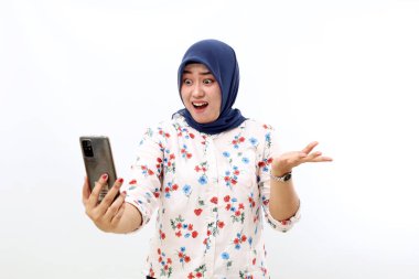 Shocked asian muslim woman standing while holding a cell phone. Isolated on white background