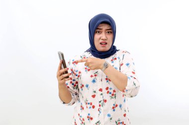 Disappointed asian muslim woman holding a cell phone while pointing on it, Isolated on white