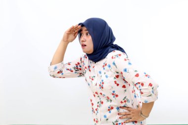 Asian muslim woman looking far away at distance with hand over head. Vision concept.