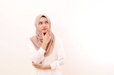 Düşünceli genç Asyalı Müslüman kadın bir şey düşünürken ayakta duruyor. Beyaz arkaplanda izole